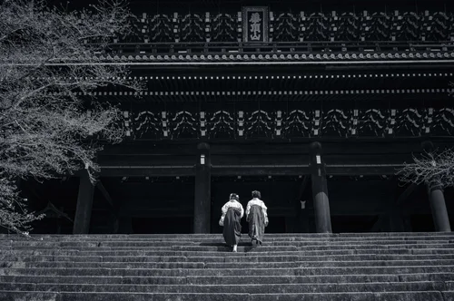 Two figures in kimono climbing the broad steps to a great temple hall, Kyoto, in black and white.