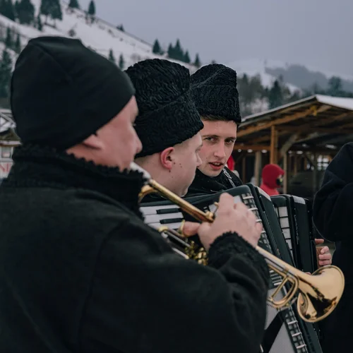 Musicians in dark coats and hats playing brass horns at a winter gathering, Bucovina, Romania.