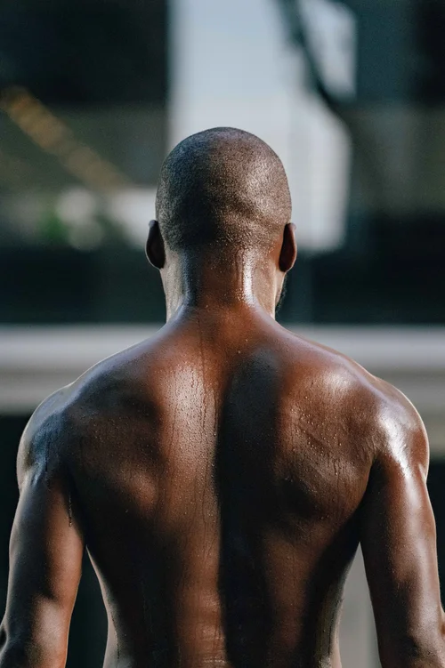 A dancer seen from behind, bare shoulders and shaved head lit in warm light against a softly blurred background, Miami.