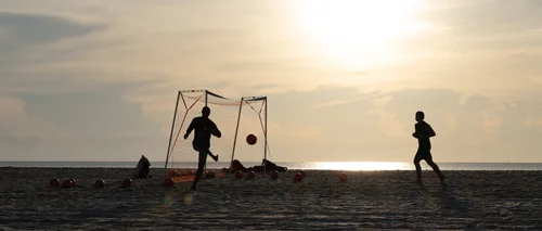 Figures playing football beside a goal on the sand, silhouetted against the rising sun, Miami Beach.