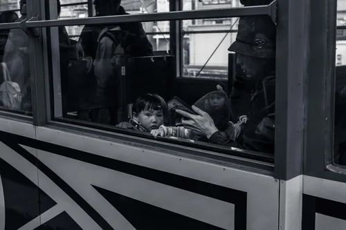 A child gazing out through the window of a bus, others behind the glass, Kyoto, in black and white.