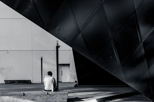 A lone figure standing beneath the dramatic dark angular canopy of the Contemporary Jewish Museum in San Francisco, dwarfed by the architecture in black and white.