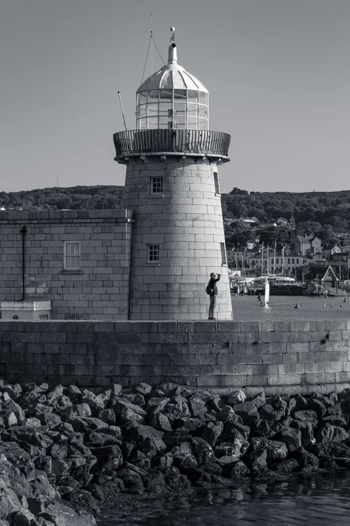 The whitewashed lighthouse at the end of Howth harbour pier in Dublin, standing over the rocky breakwater in black and white.