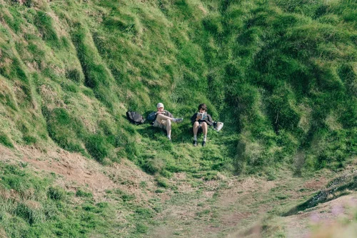 Two people sitting together on the lush green slope of Howth Head, Dublin, cradled by the overgrown hillside.
