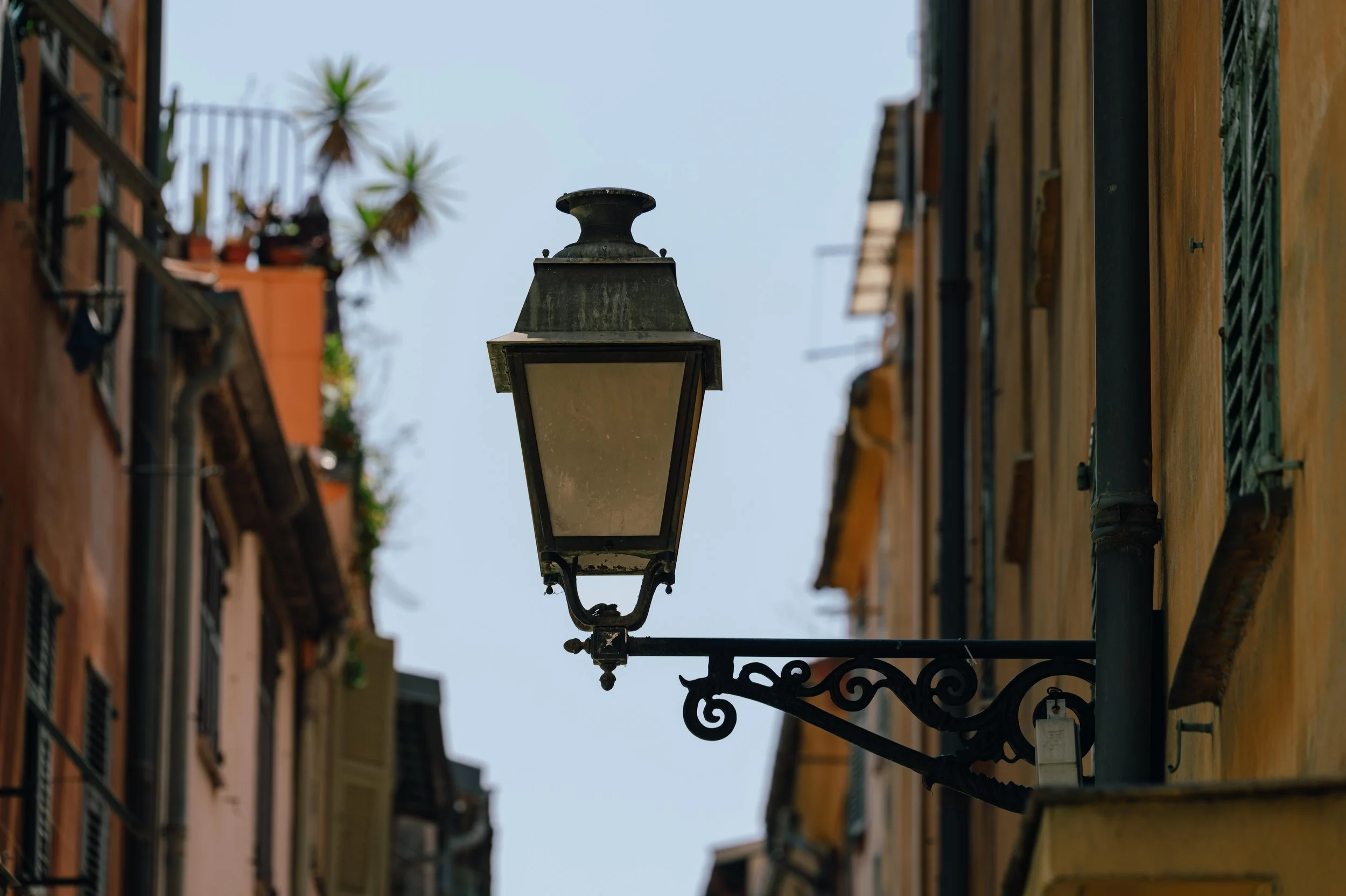 A wrought-iron street lantern on an ornate bracket between tall ochre buildings in the old town of Nice.