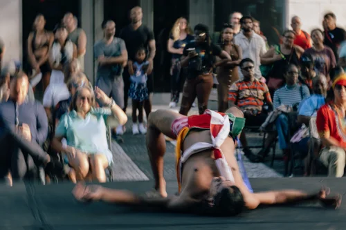 A dancer reclined on the ground in a red garment before a close ring of seated onlookers, Miami.