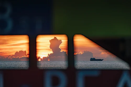 A sunrise reflected across the glass panes of a beach structure, the sky and a distant ship mirrored in each pane, Miami Beach.