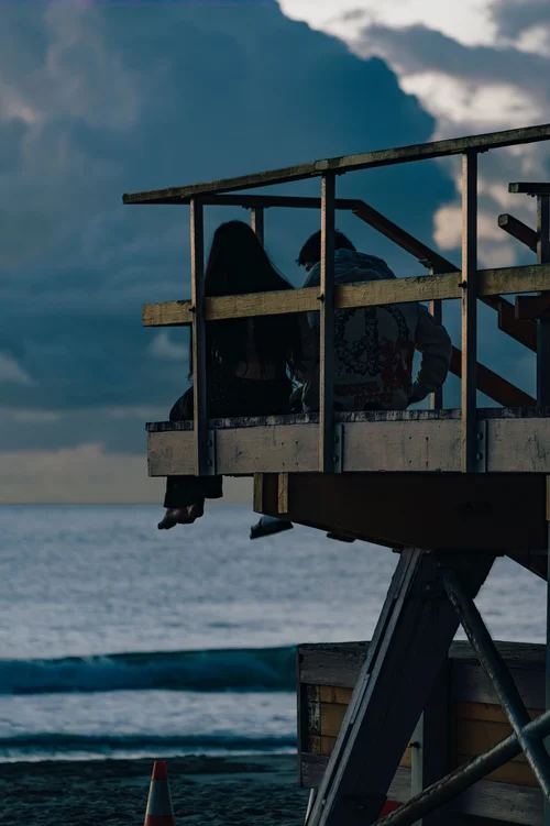 People gathered on a lifeguard tower silhouetted against a moody blue sky above the surf, Miami Beach.