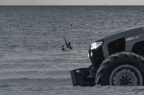 A beach tractor at the water's edge, a figure in the shallows beside it, Miami Beach.