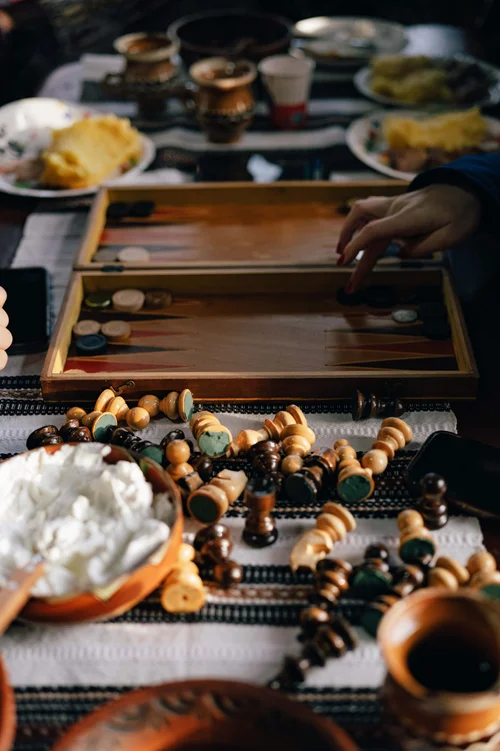 A wooden backgammon board set out on a table with drinks and food around it, seen from above, Bucovina, Romania.