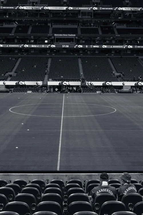 Black and white view of an empty football stadium from the stands, the pitch and rows of seats below the scoreboard
