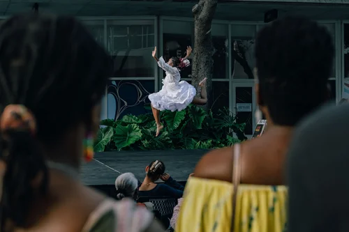 A dancer in a white dress leaping in the distance, framed between two onlookers in the foreground, Miami.