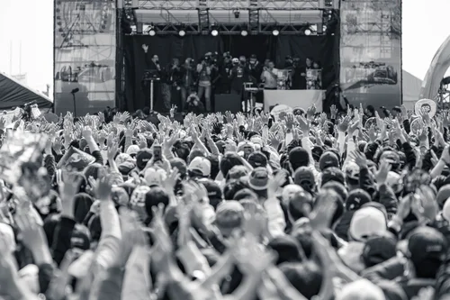 Black and white photo of a band on an outdoor festival stage with a dense crowd raising their hands in front