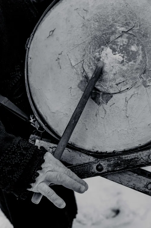 A close view of hands beating a large drum with mallets at a winter celebration, Bucovina, Romania, in black and white.