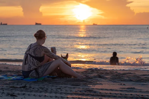 A person sitting on the sand watching the sun rise over the sea, its light spilling across the water, Miami Beach.