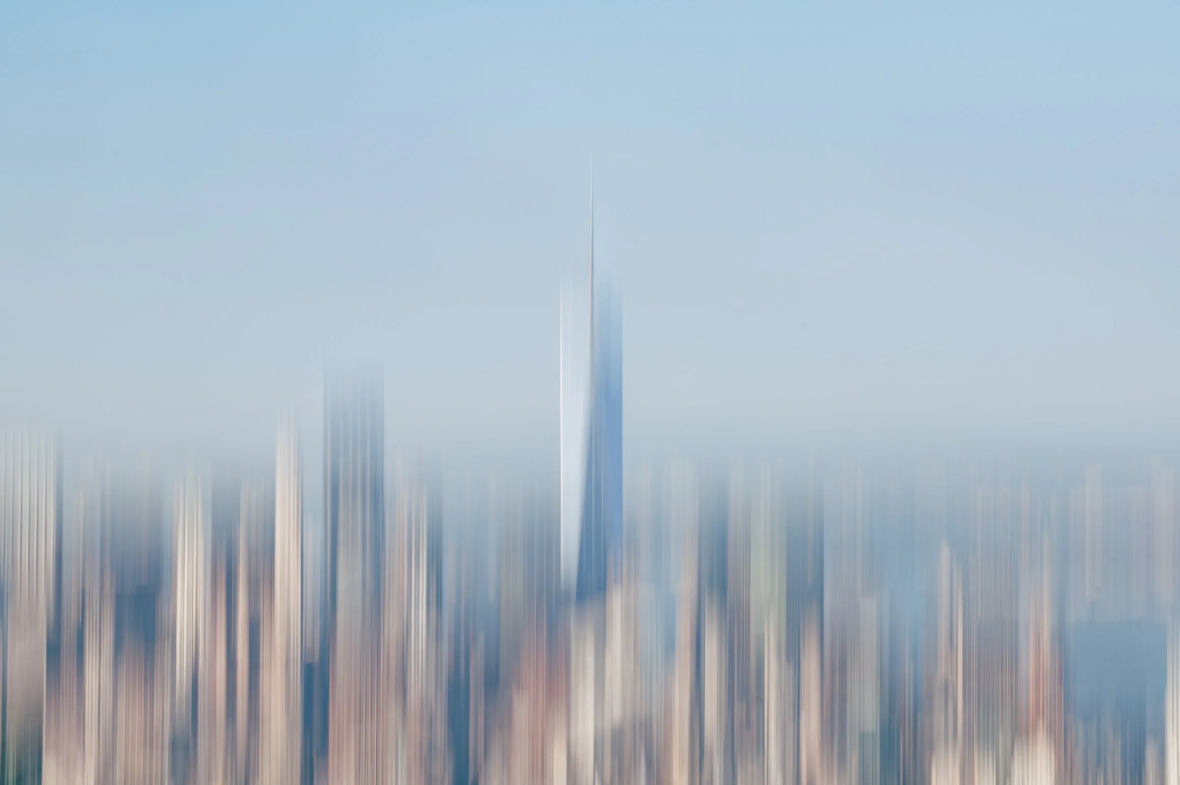 The downtown skyline pulled into fine vertical streaks by a moving camera, one tall tower still readable as a pale shaft against blue.