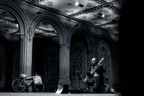 A lone musician playing beneath the grand tiled arches of Bethesda Terrace in Central Park, New York, a bicycle parked nearby, in black and white.