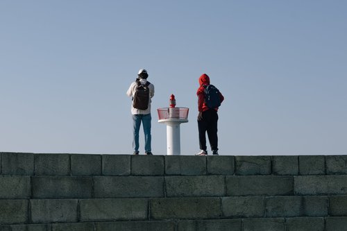 Two people standing on top of a stone harbour wall at Howth, Dublin, looking out under a clear blue sky.