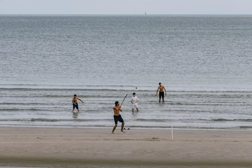 People spread across the wet sand at low tide on Portmarnock beach, Dublin, some playing on the flat expanse where the sea has drawn back.