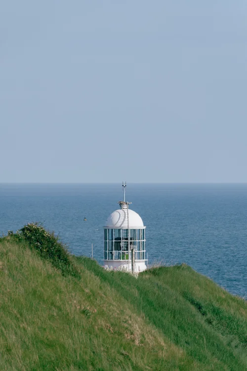 A small white lighthouse on the grassy headland at Howth, Dublin, above the blue expanse of the sea.