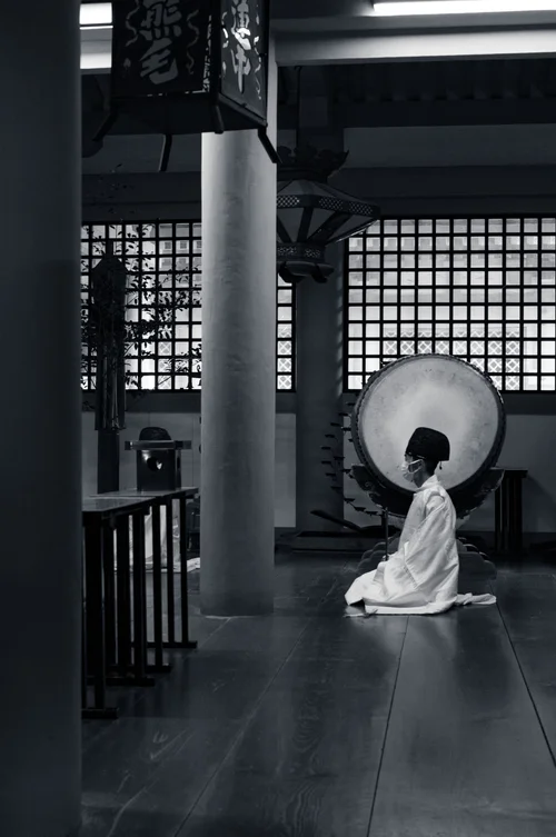 A figure in kimono with a round parasol seen from behind, looking out from a temple veranda, Miyajima, in black and white.