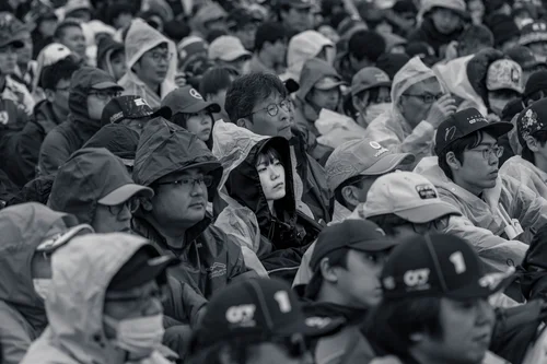 Black and white photo of a packed crowd of spectators in rain ponchos and team caps watching intently