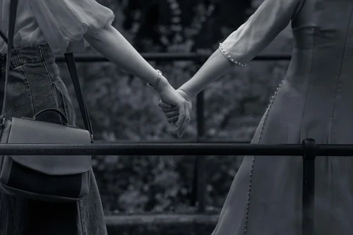 Two people in kimono holding hands by a railing, a close view from the side, Kyoto, in black and white.