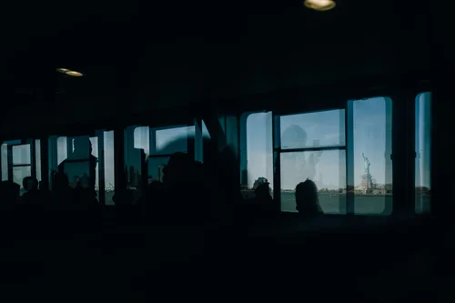 Silhouetted passengers seated against the glowing windows of a dark train interior at dusk in New York.