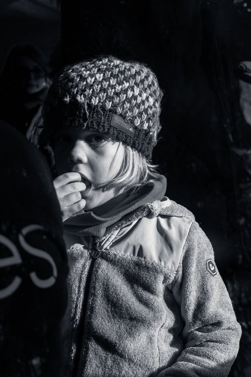 A black and white portrait of a person in a patterned knit hat, hand raised to the face against the cold, Bucovina, Romania.