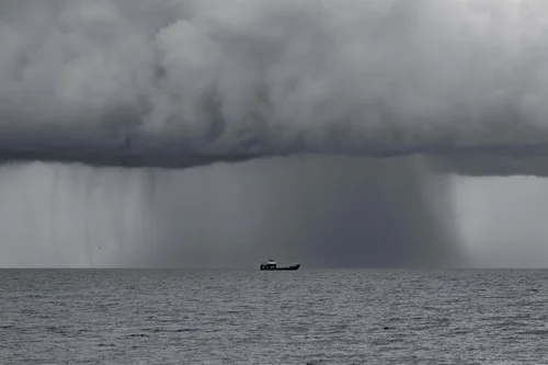 A curtain of rain falling from a heavy storm cloud over the sea, a small boat beneath it, Miami Beach.
