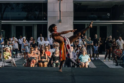 A dancer performing in a flowing red garment before a seated audience in an urban plaza, Miami.