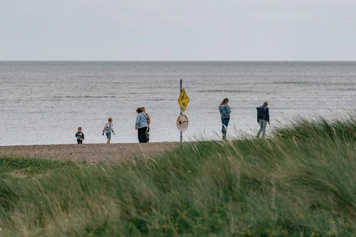 A group of people gathered on the beach at Malahide, Dublin, standing among the dune grass by a marker flag with the wide strand behind.