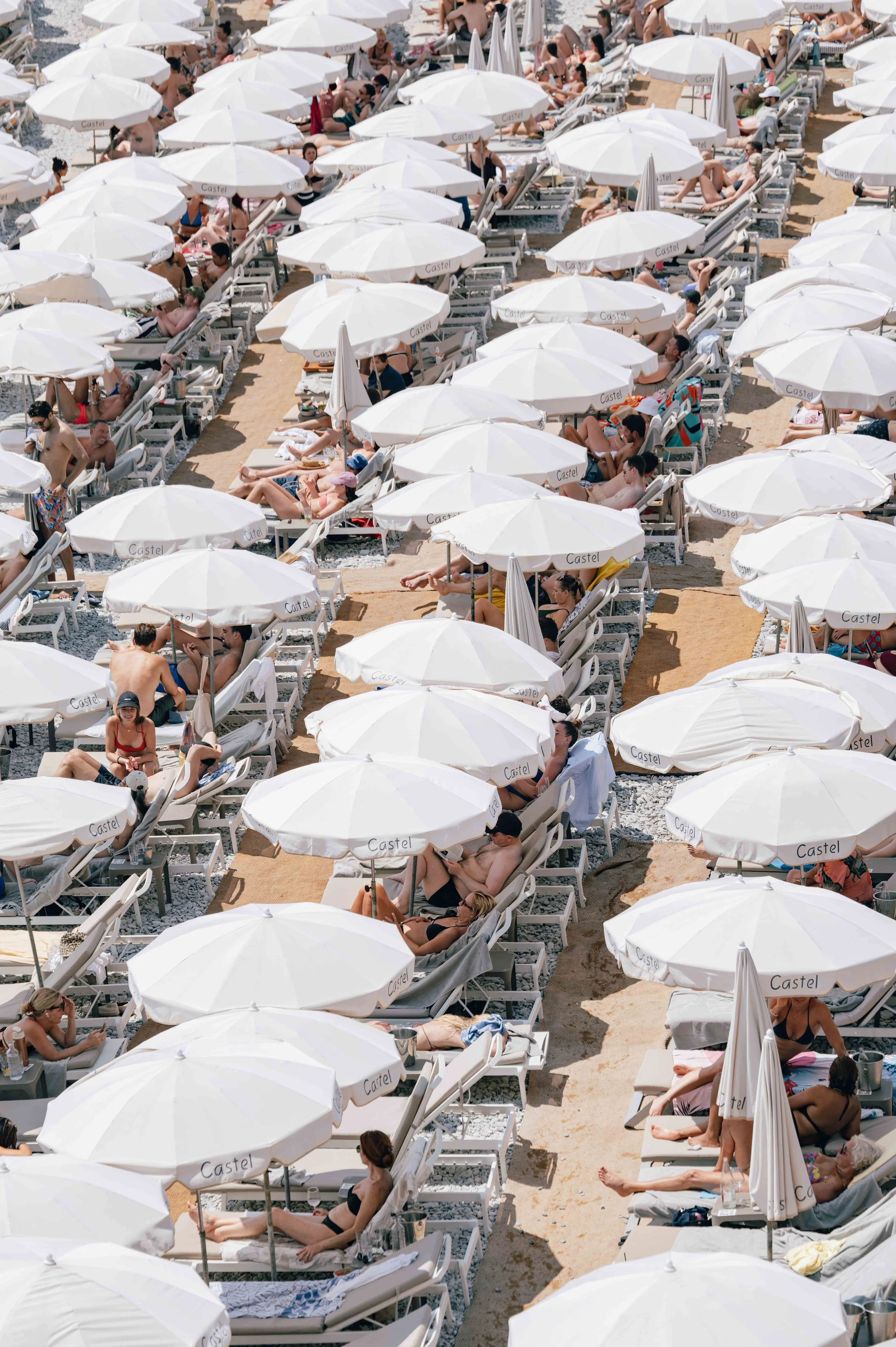 Rows of white parasols and sun loungers seen from above on a packed beach along the Baie des Anges in Nice.