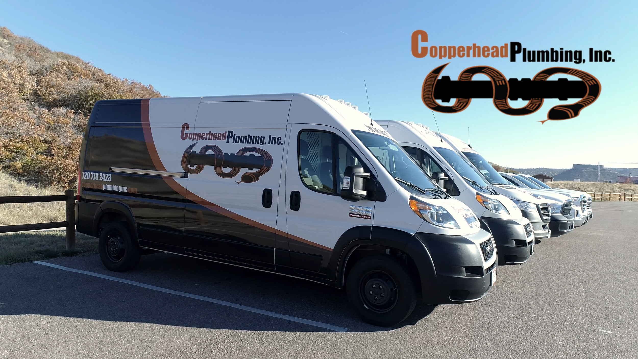 A row of White service vans with the Copperhead Plumbing, Inc. logo parked in a parking lot with a scenic hilly landscape in the background.