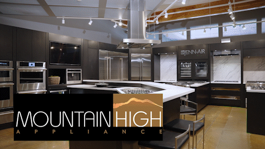 Modern kitchen showroom with dark cabinets, stainless steel appliances, and a central island, displaying the Mountain High Appliance logo.