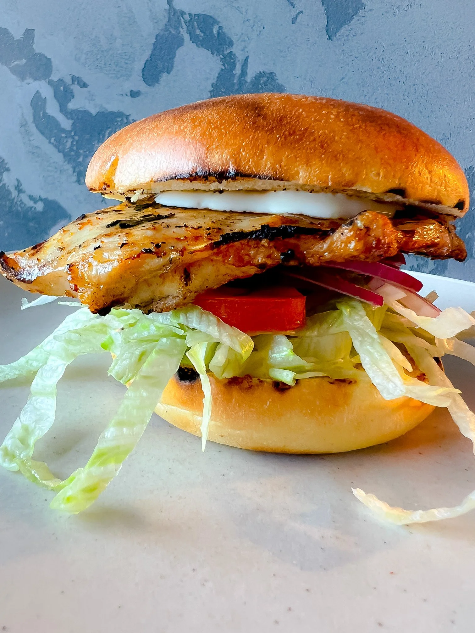 Close-up of a grilled chicken sandwich with lettuce, tomato, pickles, grilled chicken breast, mayonnaise, and a toasted bun.