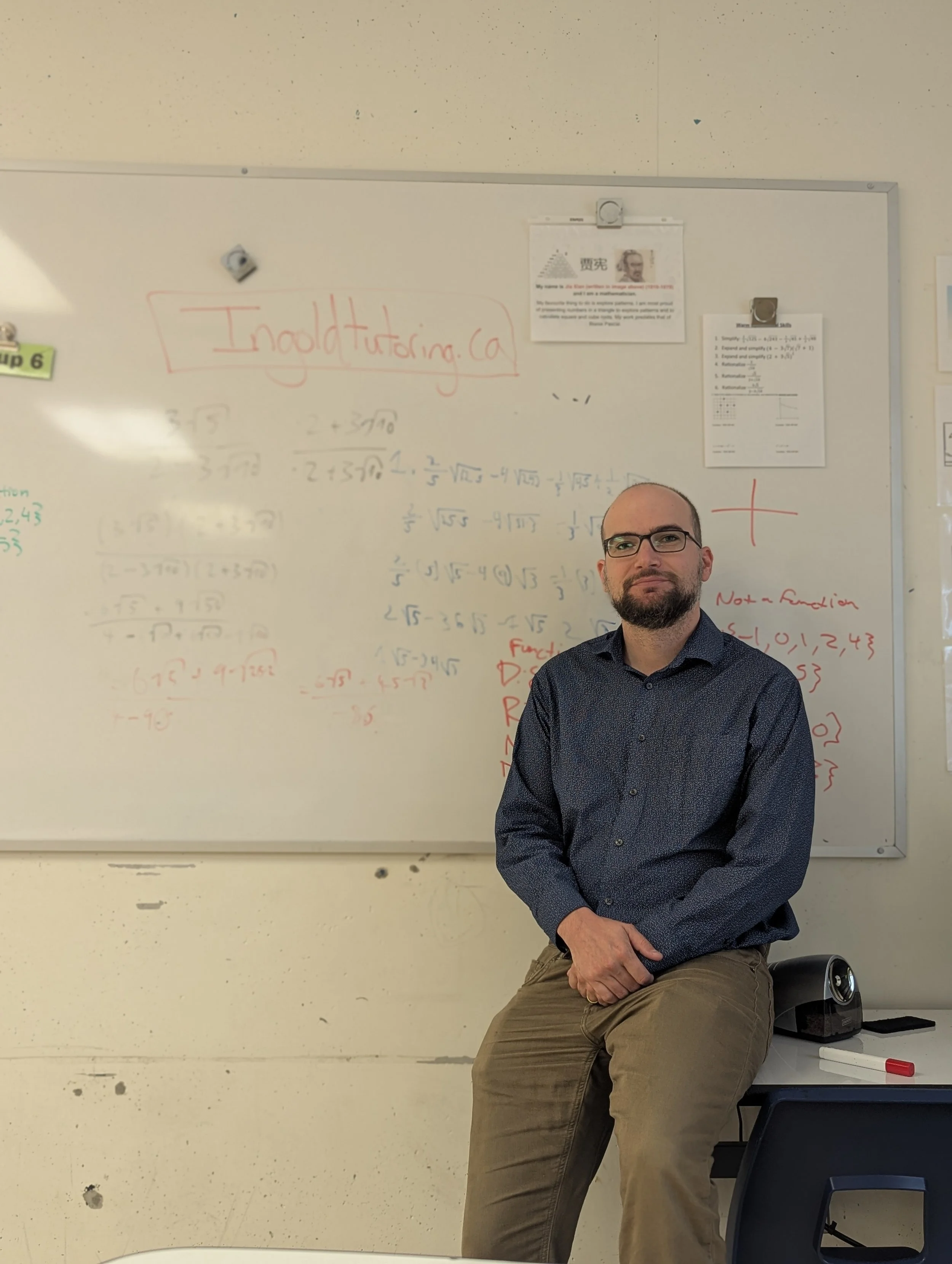 Andrew Ingold, Certified Ontario Teacher, sitting at a classroom desk with ‘Ingold Tutoring’ written on the board – offering online math and science tutoring in Hamilton, Halton, and across Ontario.