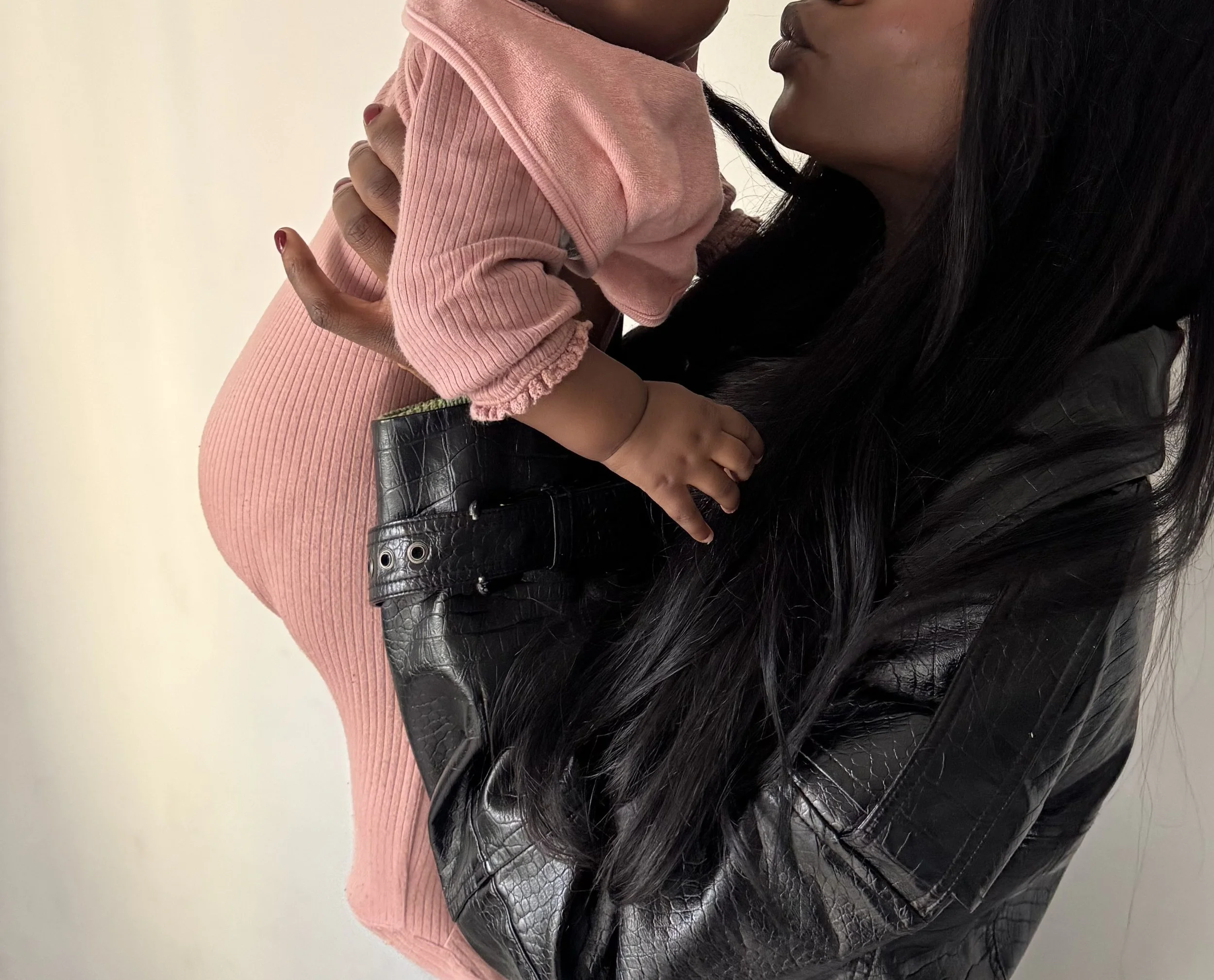 A woman holding a young child, focusing on their torsos and faces, with the woman wearing a black leather jacket and the child in a pink corduroy outfit.