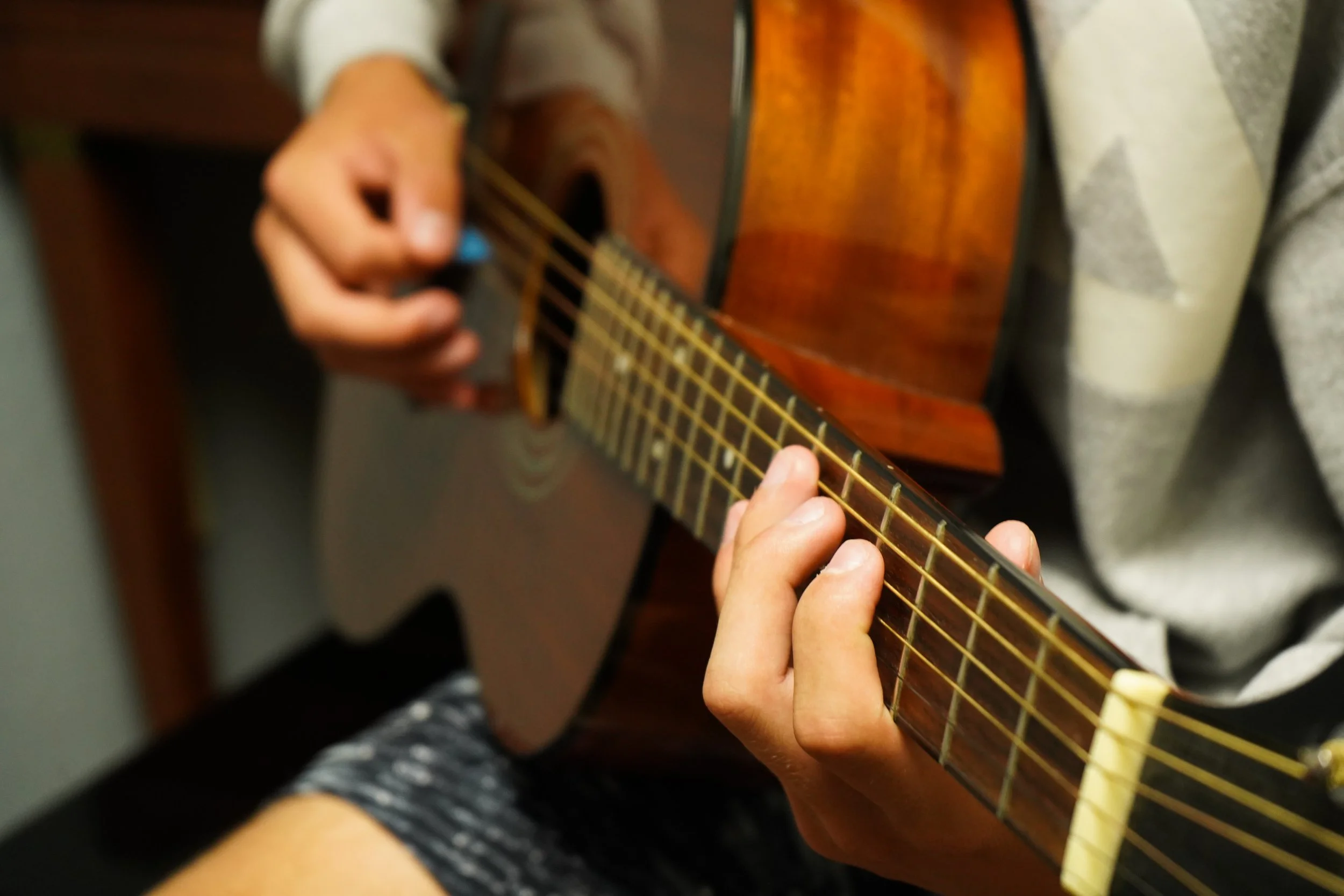 A person playing an acoustic guitar, focusing on their hands on the fretboard.