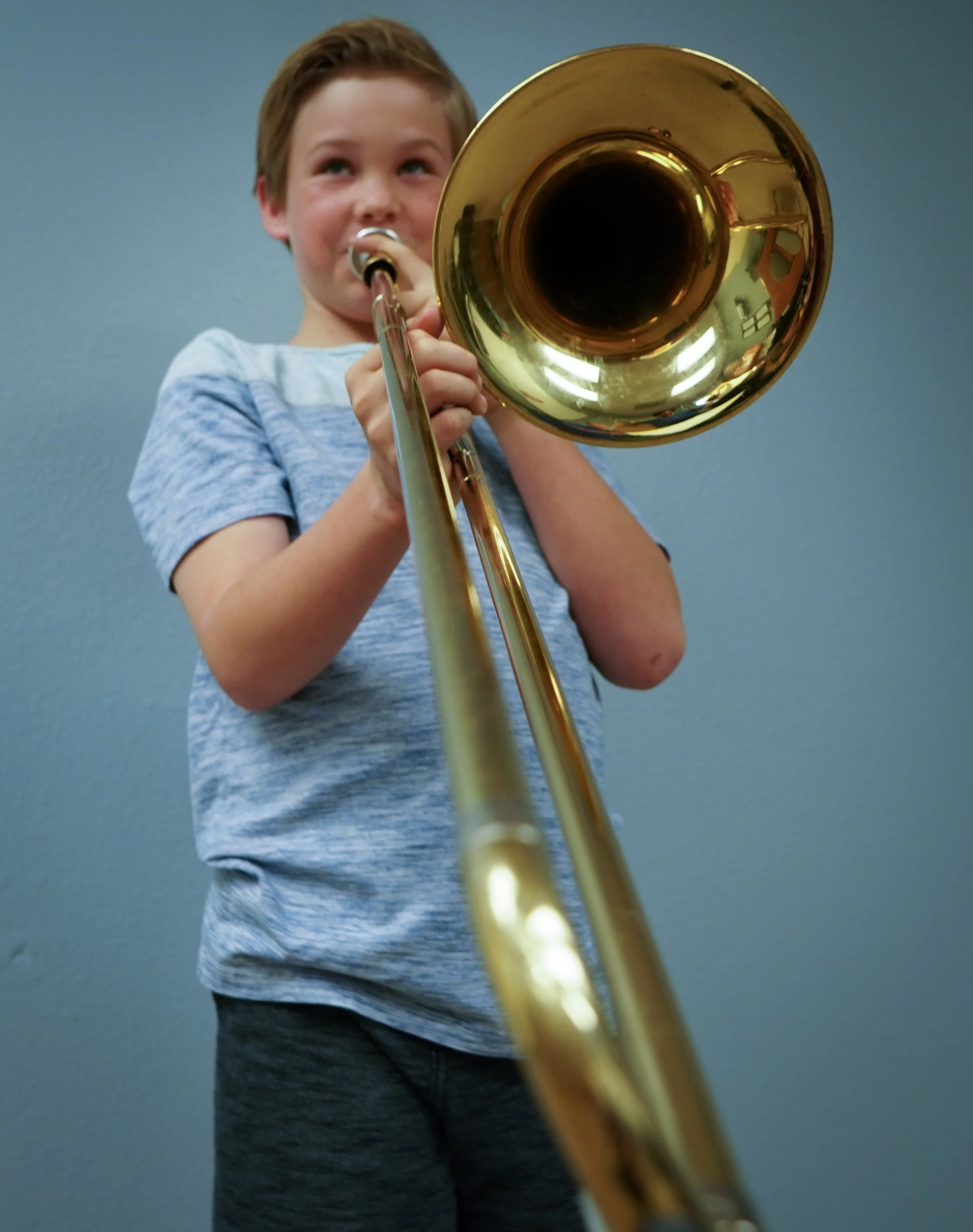 Young boy playing trumpet, viewed from below, with a plain wall background.