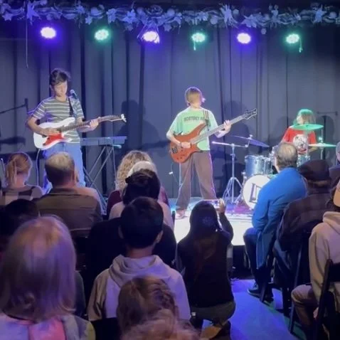 Young band performing on stage with audience watching.
