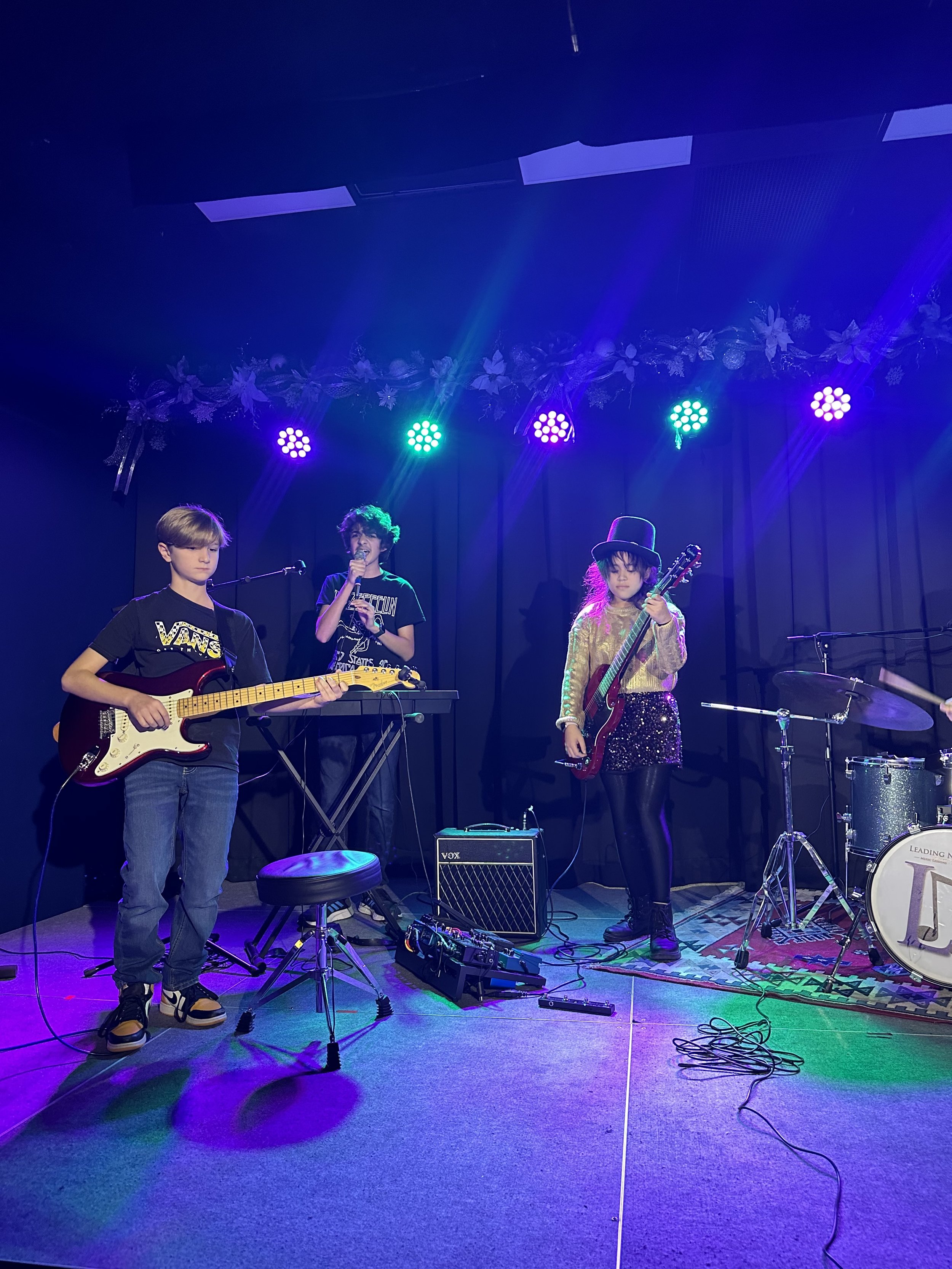 Children performing a music concert on stage with colorful lights, musical instruments, and microphones.