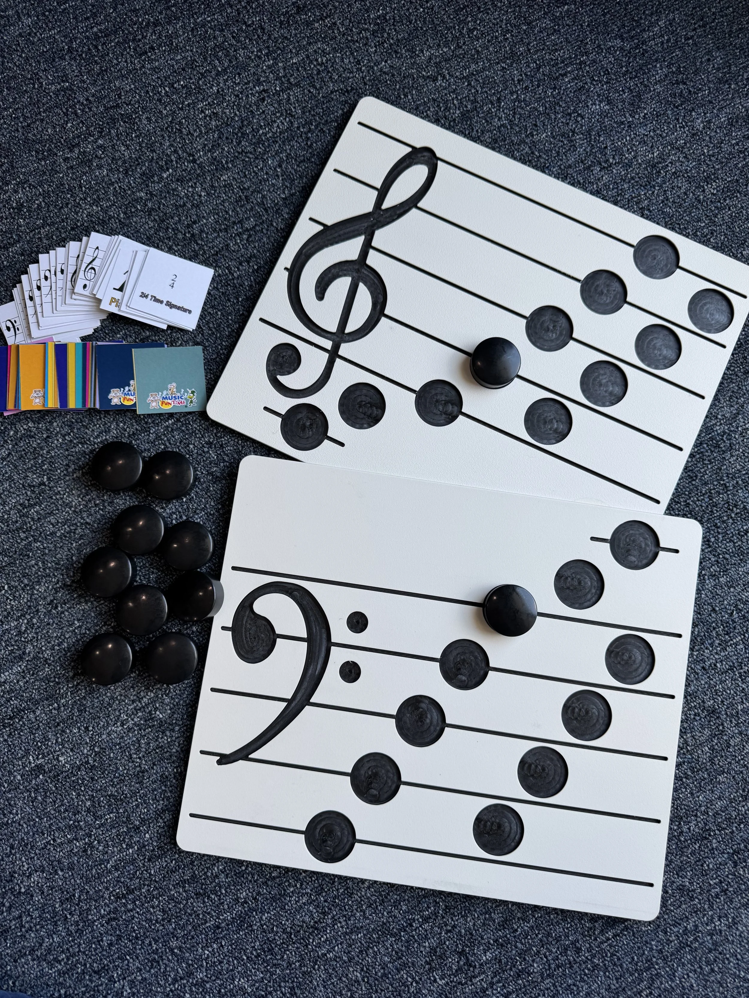 Musical note bingo game setup with two boards, black bingo balls, and small cards for calling out notes, on a dark surface.