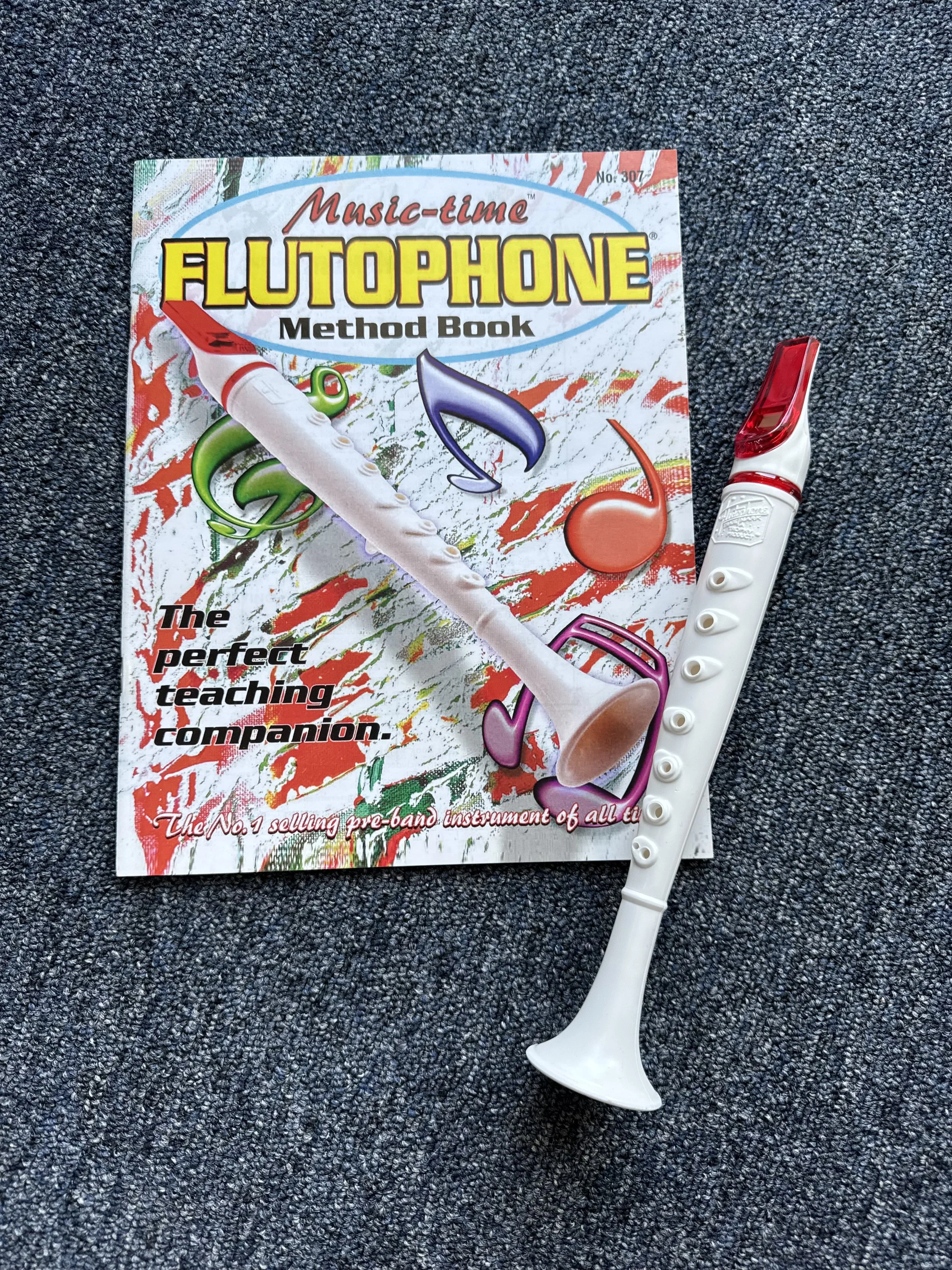 Music time Flutophone method book, colorful cover with musical notes and a white flutophone, placed on a dark textured surface.