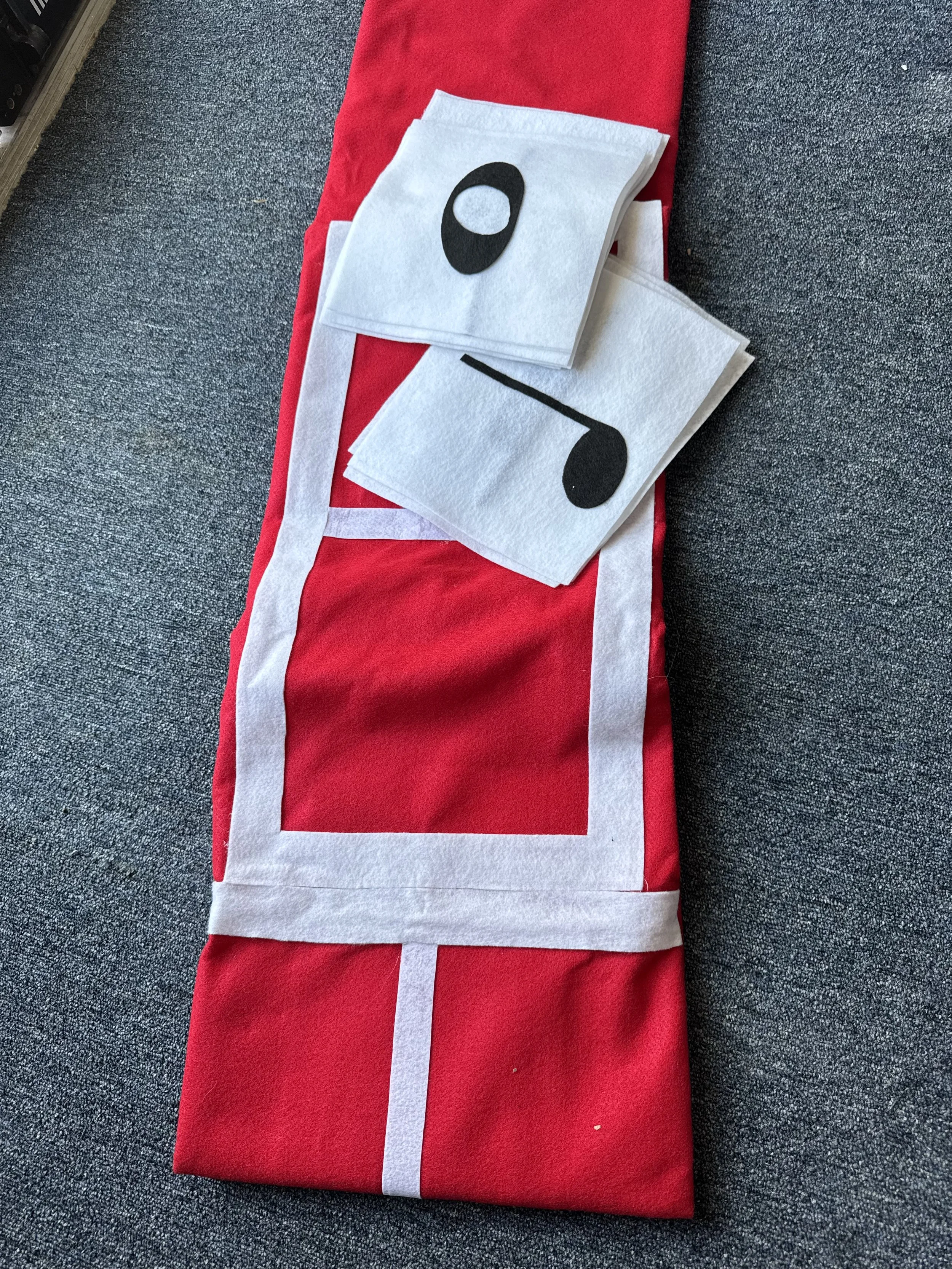 Felt Christmas stocking with white trim and a red body, placed on a gray carpet, with two white felt tissue paper pieces with black musical note and circle designs on top.
