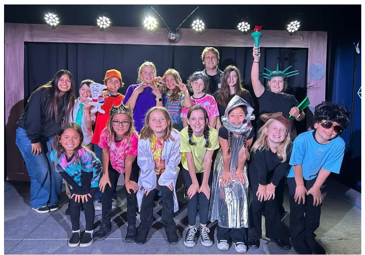 A group of children and an adult on a stage dressed in costumes for a theater production of 'School House Rock Live!' at a school in Spring 2025.