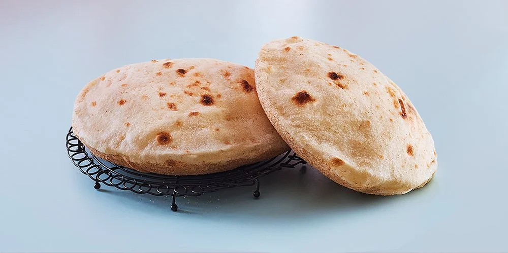 Two pieces of naan bread on a metal stand against a light blue background.