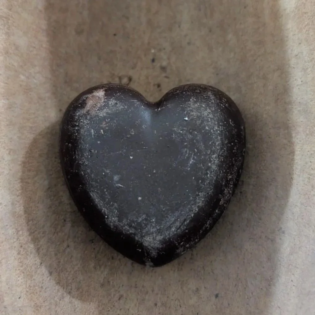 A smooth black heart-shaped stone on a tan surface.