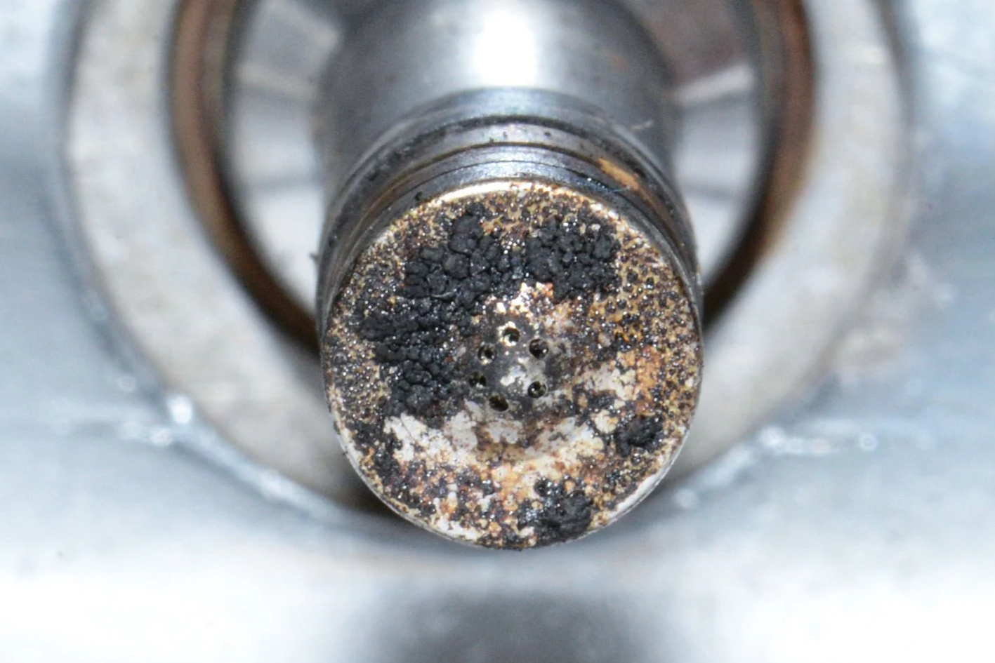 Close-up of a rusty metal part with black corrosion and residues.