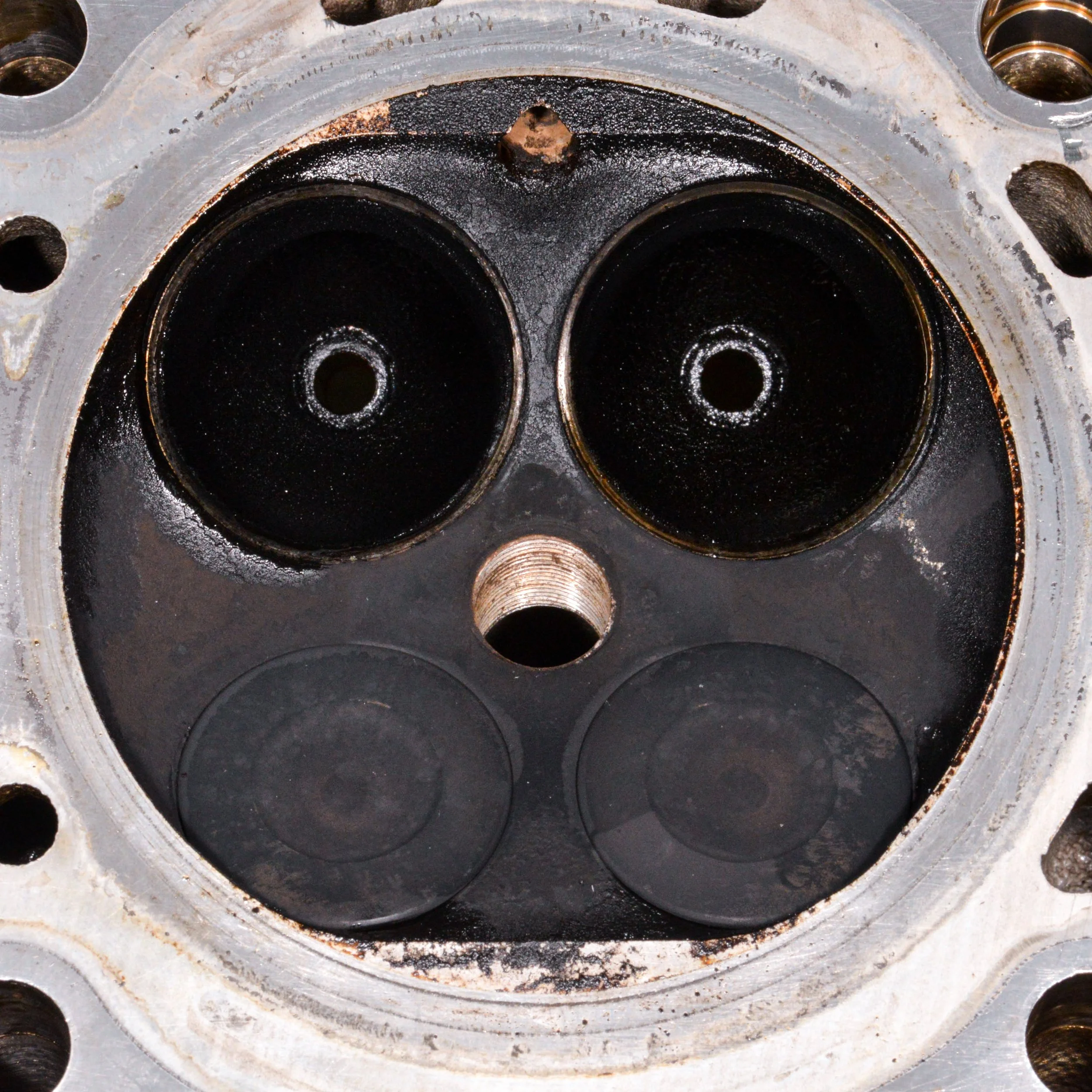 Close-up view of a car engine cylinder head with four black valves and one threaded spark plug hole.